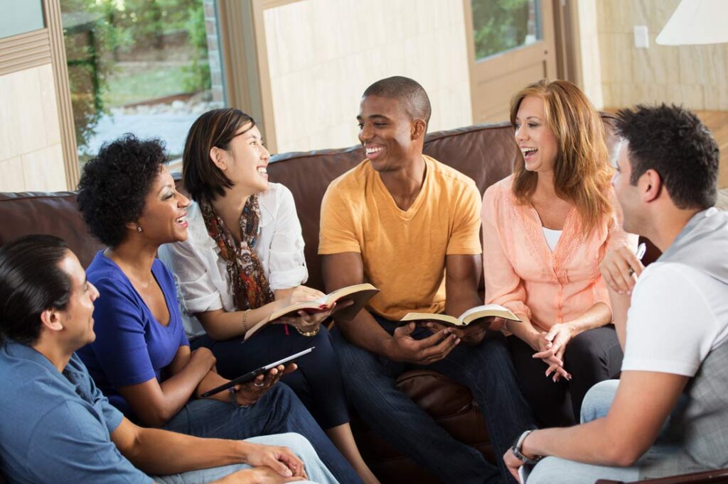 Group of people holding books sitting on a couch smiling in a bibliotherapy therapeutic book club