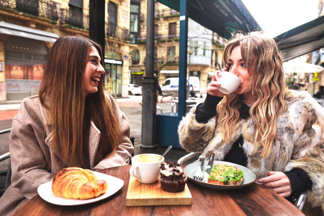 Two women in their 30s drinking lattes and eating avocado toast to exemplify Money Mistakes Millennials Make