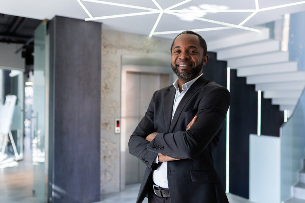 Black male executive in a suit with his arms crossed smiling because he keeps up with personal and professional development trends