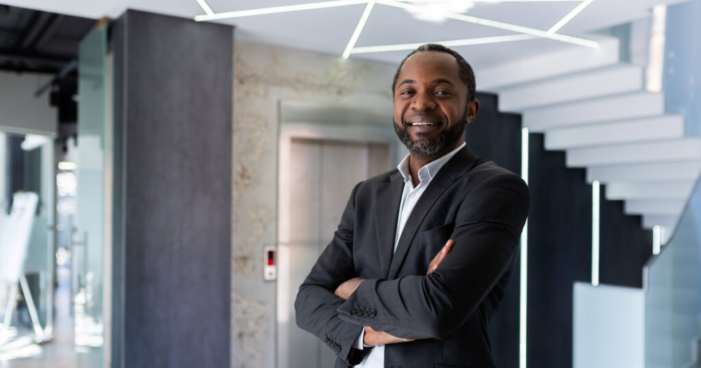 Black male executive in a suit with his arms crossed smiling because he keeps up with personal and professional development trends