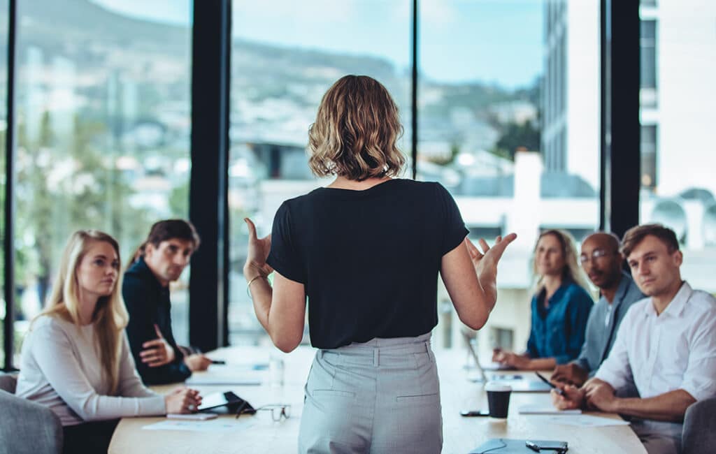 Rear view of a woman speaking to a group of employees at a conference table