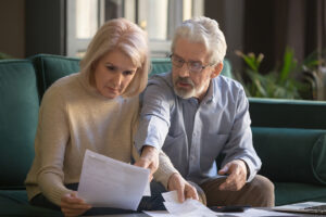 Serious grey haired mature couple calculating bills, checking finances together at home