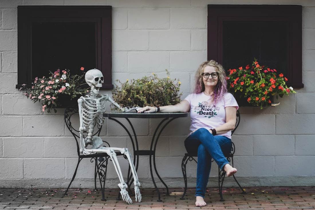 Amy Pickard, who throws death parties, holding hands with a faux skeleton at a bistro table