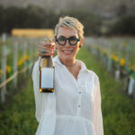 Sommelier in a vineyard holding a bottle of wine exemplifying women in wine