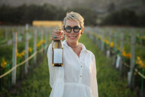 Sommelier in a vineyard holding a bottle of wine exemplifying women in wine