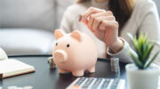 Young woman saving money monthly expenses putting coin in to piggy bank on the table.