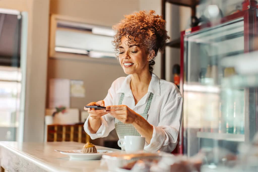 Female business owner taking a picture of the food she made using a smartphone in her cafe