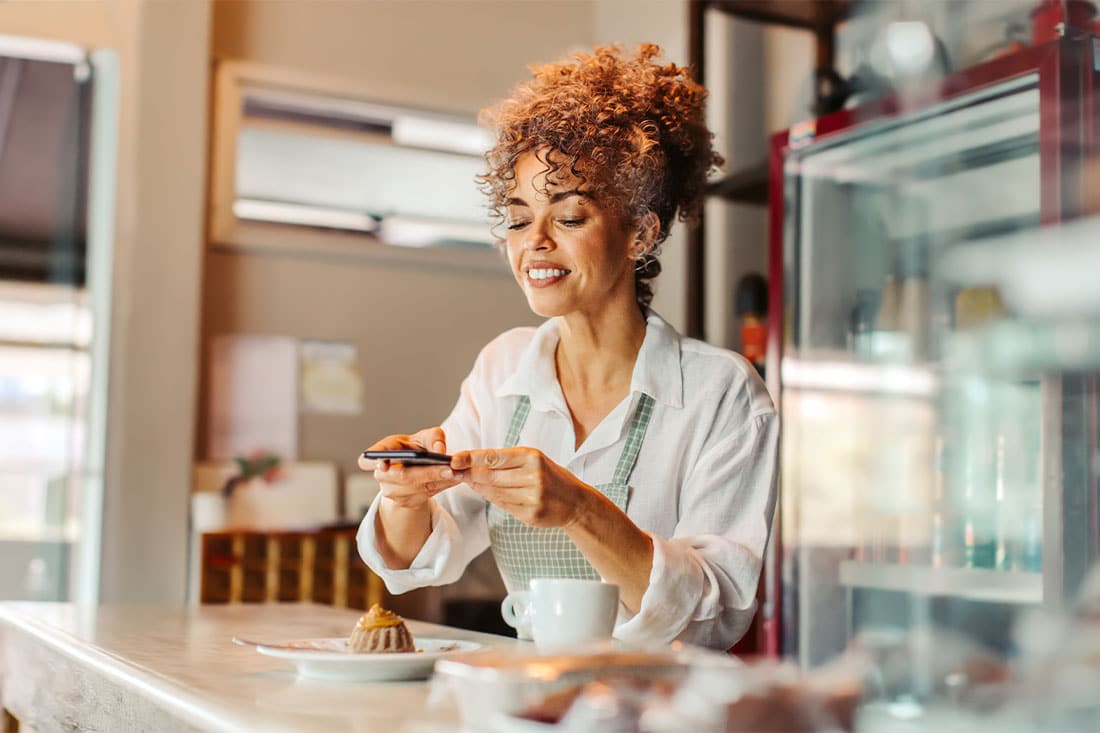 Female business owner taking a picture of the food she made using a smartphone in her cafe