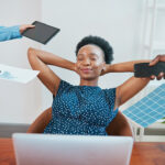 Young woman relaxes in her office while coworkers make demands, exercises boundaries