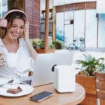 young woman using laptop and drinking coffee at restaurant terrace