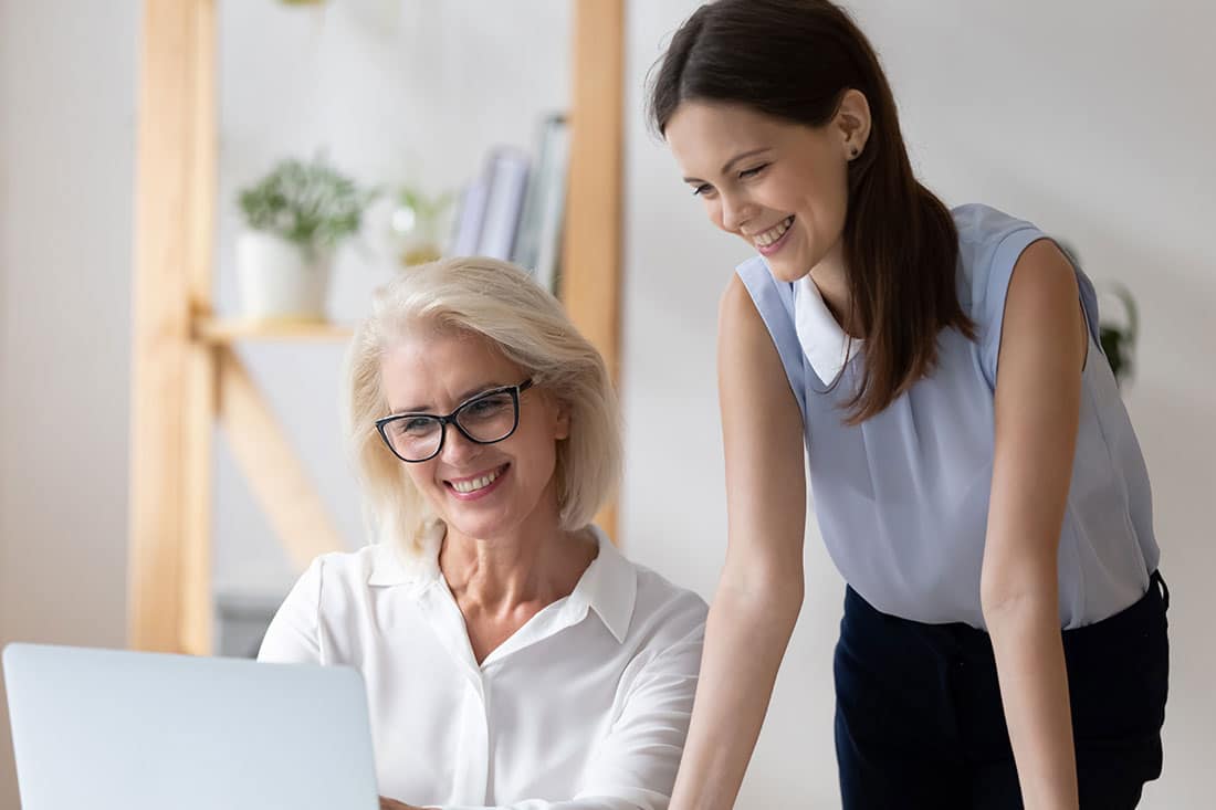 young businesswoman help middle-aged coworker with computer job at workplace