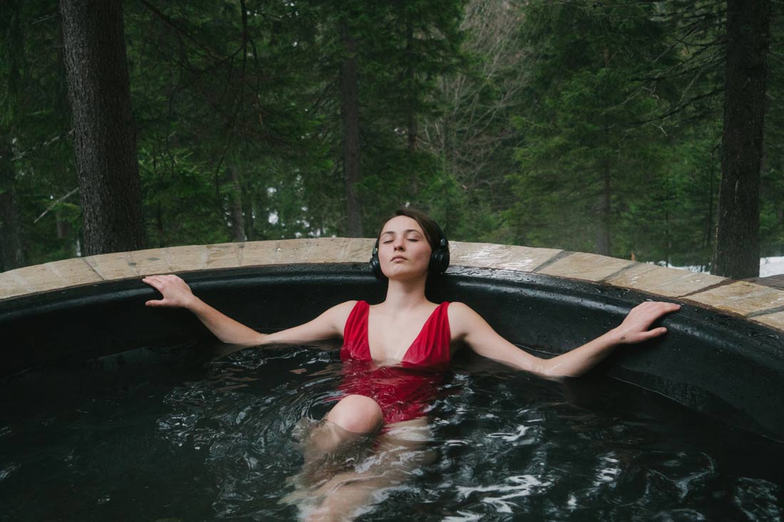 Woman listening to Myndstream on headphones in a hot tub in the woods