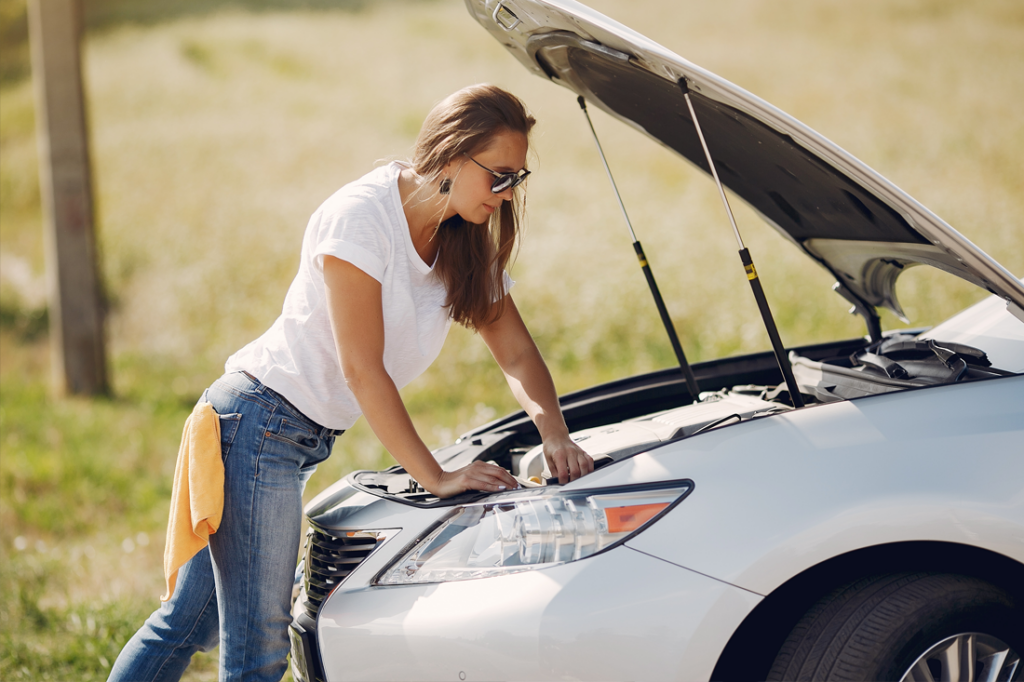 A woman in sunglasses leans over an opened car hood.