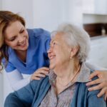 An elderly woman in a wheelchair smiles at a nurse.