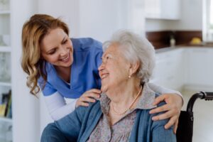 An elderly woman in a wheelchair smiles at a nurse.