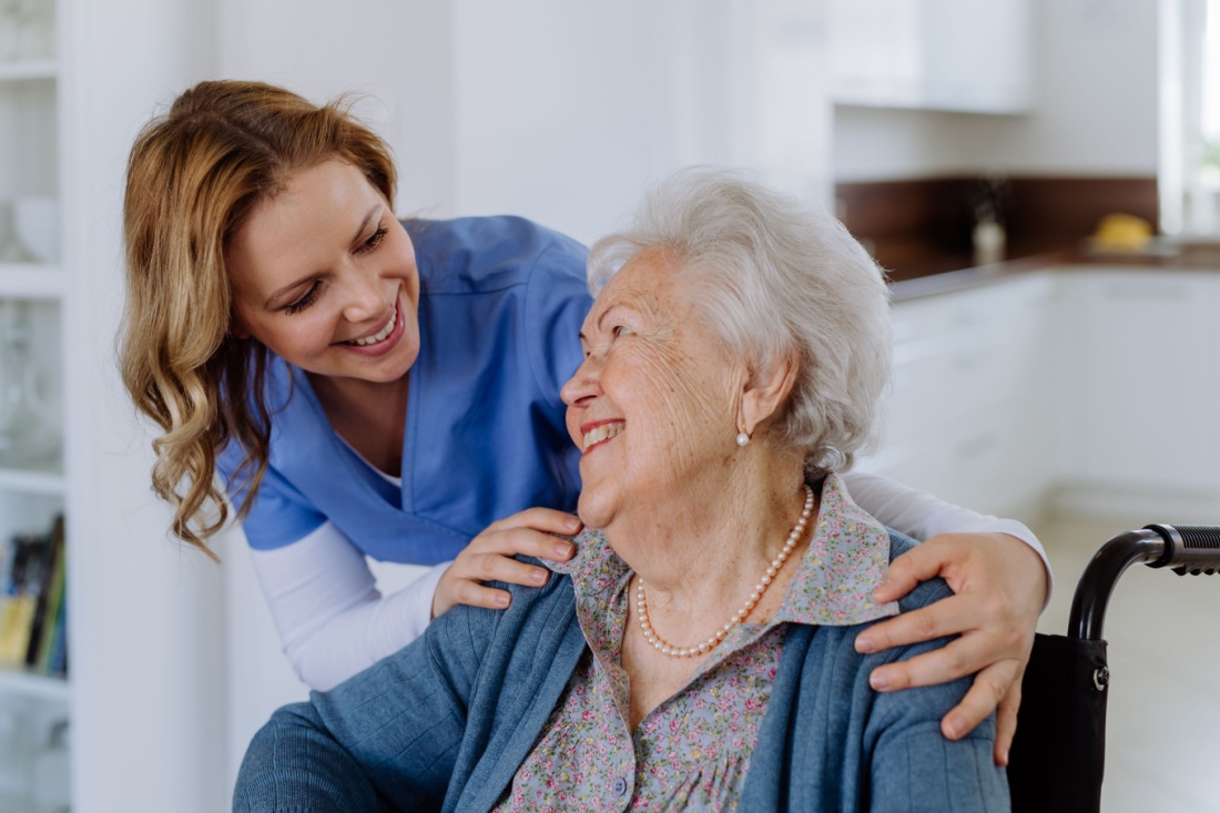 An elderly woman in a wheelchair smiles at a nurse.