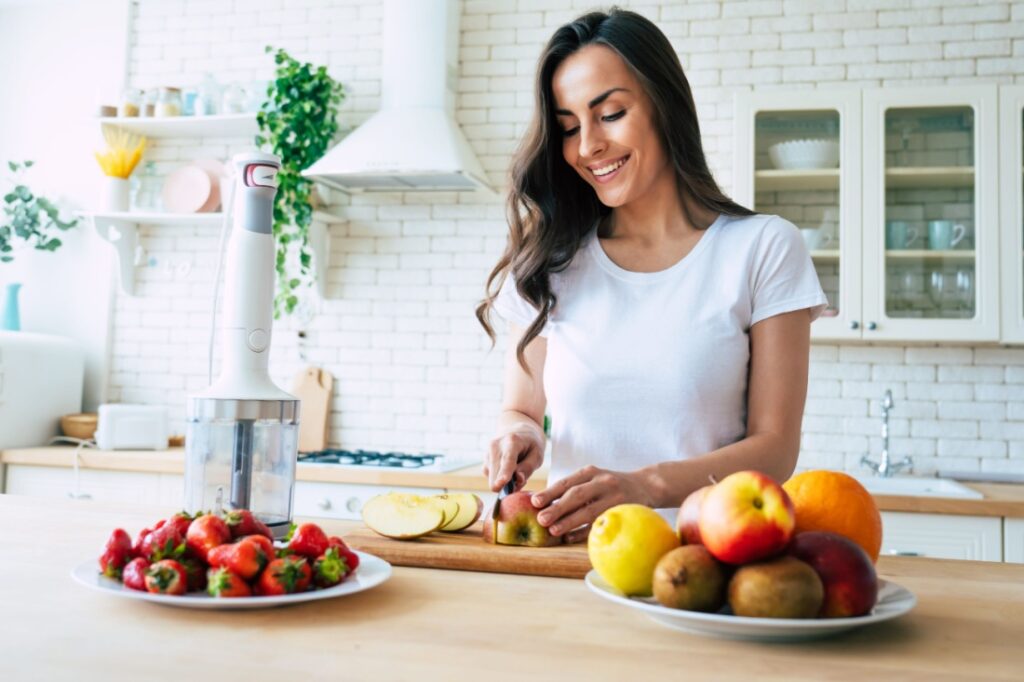 A woman chops fruit on a kitchen island.