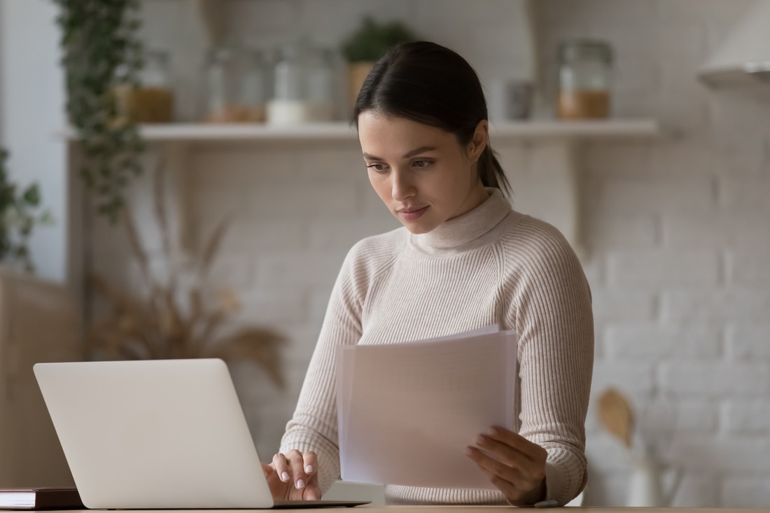 a woman sitting at a desk, using her laptop and doing paperwork