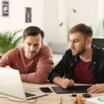 two men working on laptop in an office setting