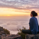 a woman sitting peacefully on a mountain