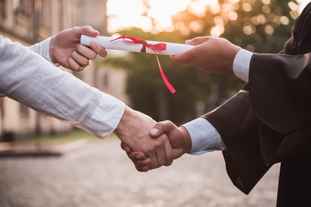 Cropped image of graduate in academic dress taking his diplomas and shaking hand, earning a degree