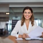 A smiling woman holds a resume and a pen.
