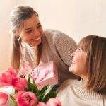 A smiling young woman presents a slightly older woman with a gift box.