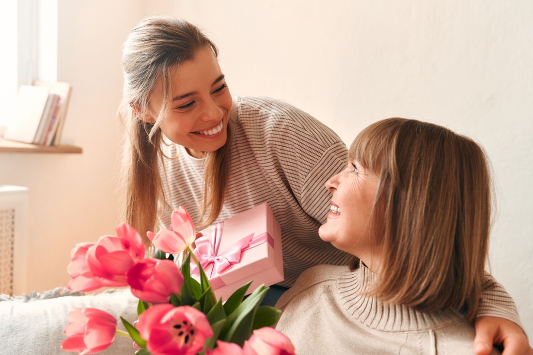 A smiling young woman presents a slightly older woman with a gift box.