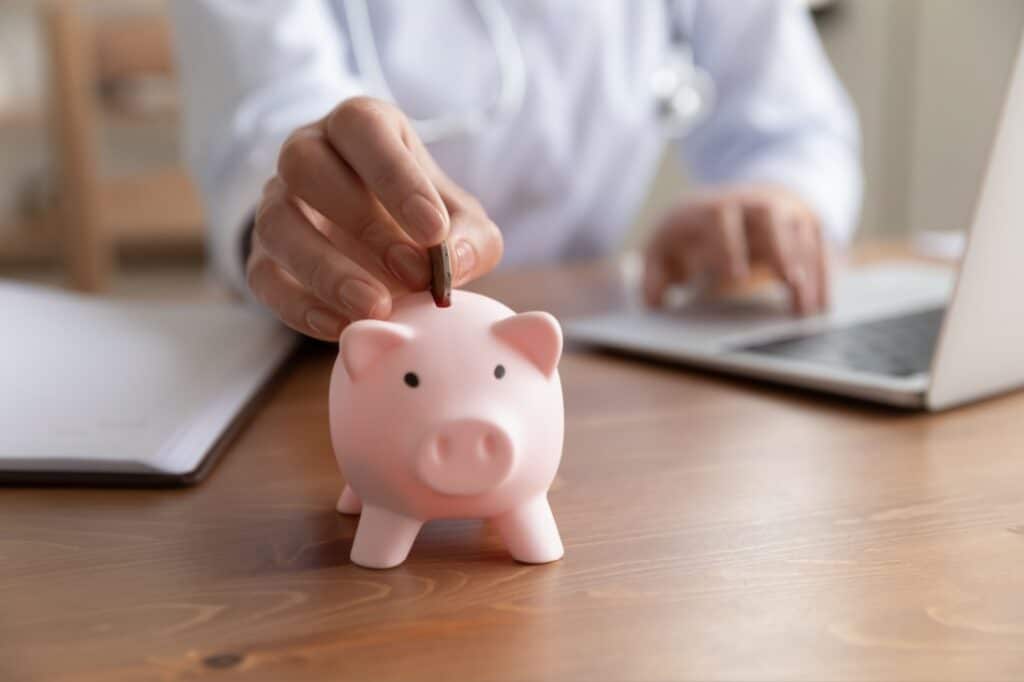 A hand deposits a coin in a piggy bank.
