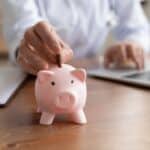 A hand deposits a coin in a piggy bank.