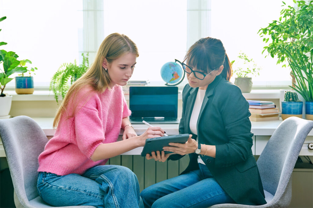 College counselor talking with teenage girl, using digital tablet for work