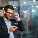 businessman in business suit uses apps on phone while smiling