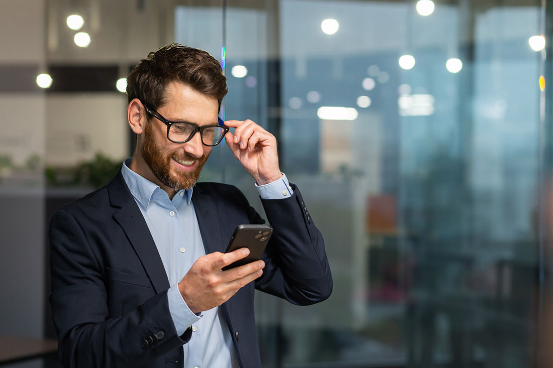 businessman in business suit uses apps on phone while smiling