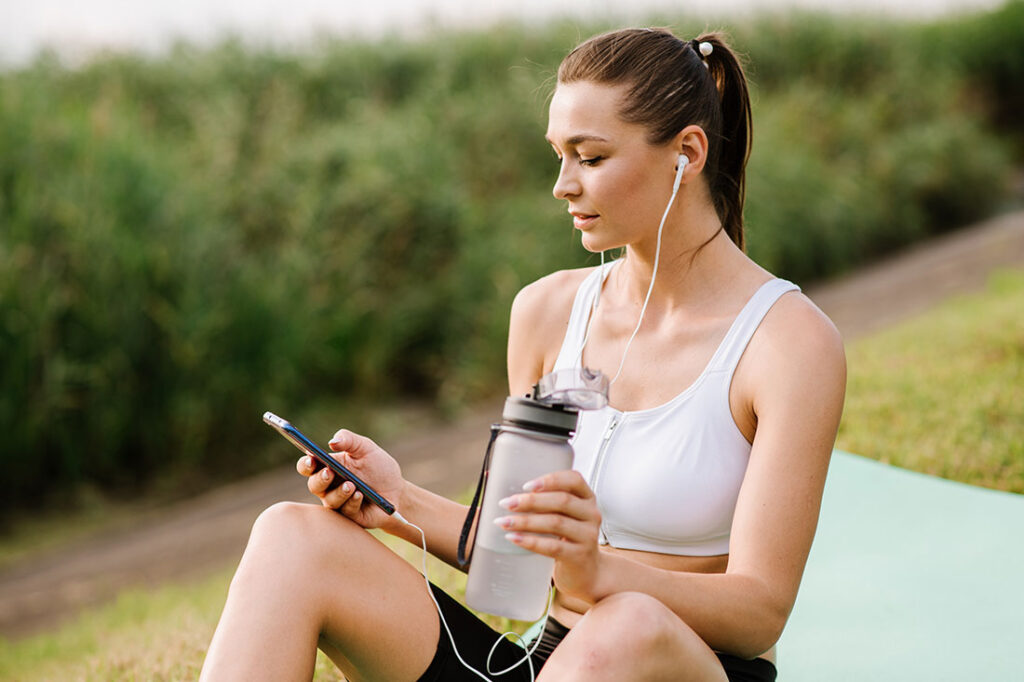 fit woman with earphones and smartphone listen music in the park at the sunny day