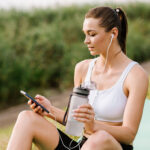 fit woman with earphones and smartphone listen music in the park at the sunny day