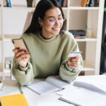 young adult student using smart phone holding a credit card
