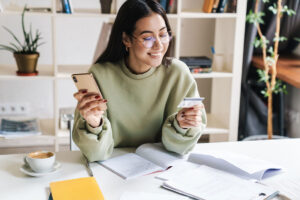 young adult student using smart phone holding a credit card