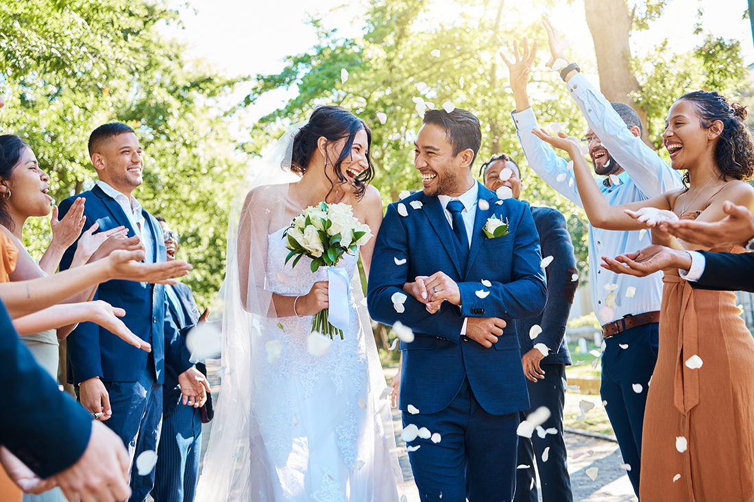 Happy, wedding ceremony and couple walking with petals and guests throw in celebration of romance. Romantic, flowers and bride with bouquet and groom with crowd of friends, family, and co-workers celebrating at outdoor marriage event.