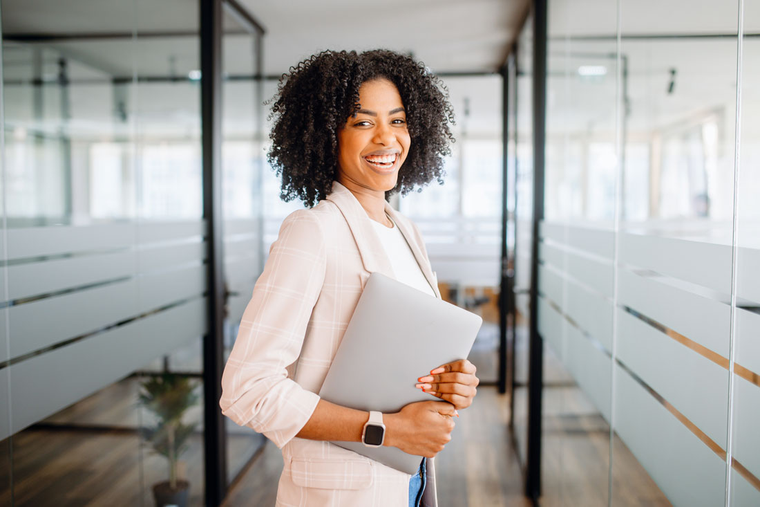 smiling woman holding her laptop where she uses productivity tools