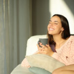 A happy woman sits on a couch and practices the power of positive thinking