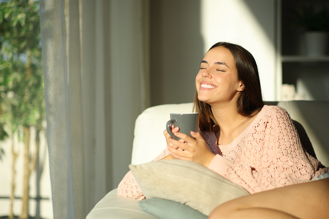 A happy woman sits on a couch and practices the power of positive thinking