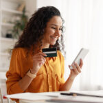 Cheerful woman using smartphone shopping online holding credit card