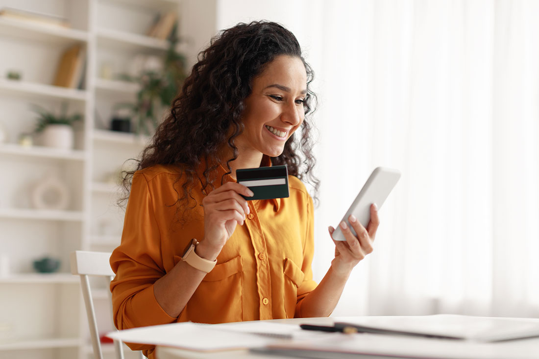 Cheerful woman using smartphone shopping online holding credit card
