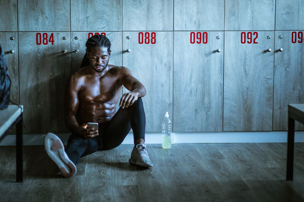 Young black athlete looking at smart phone in locker room