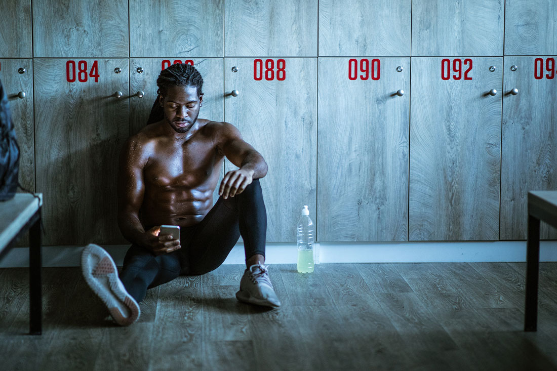 Young black athlete looking at smart phone in locker room