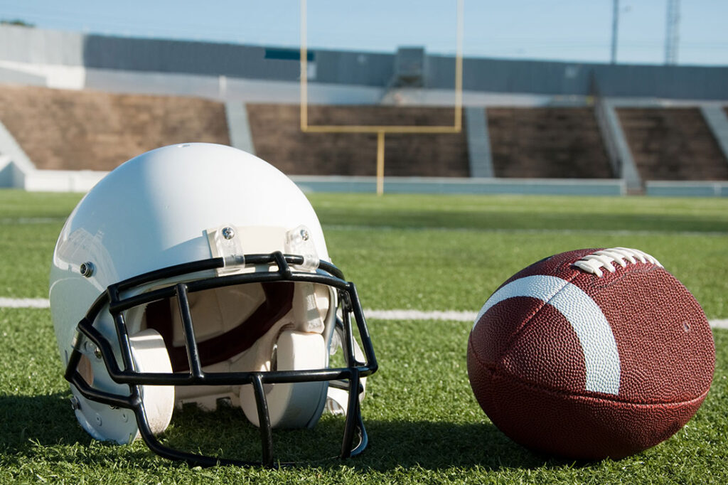 American football and helmet on field with goal post in background