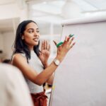 woman holding a marker near a whiteboard while speaking to a coworker