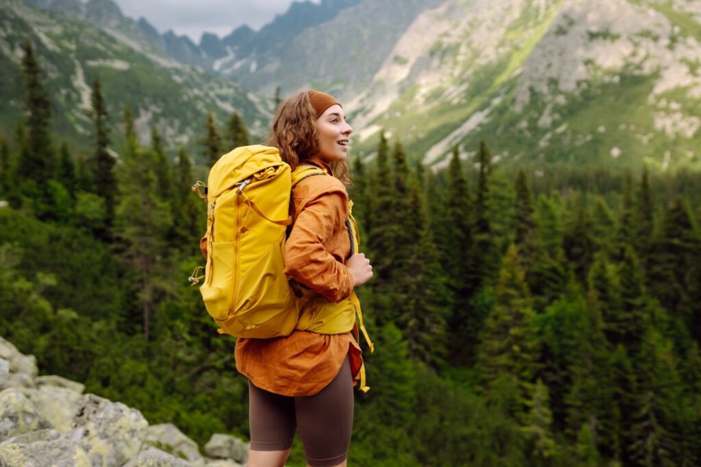 a woman hiking in the mountains while wearing a yellow hiking backpack