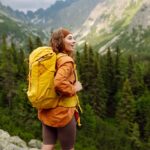 a woman hiking in the mountains while wearing a yellow hiking backpack