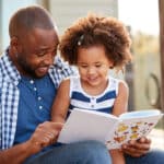 A young father enjoys reading a book aloud to his daughter